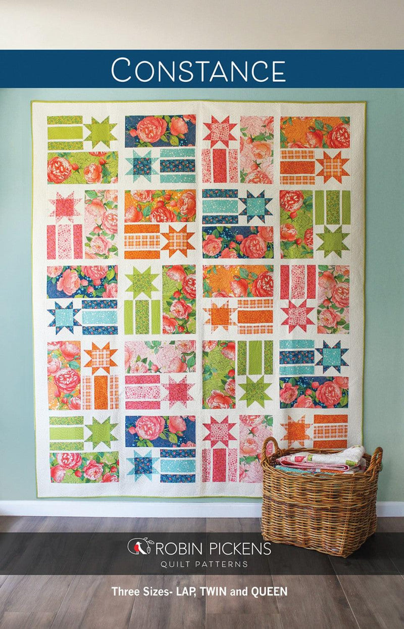 Photo: Quilt hung on a wall. Rectangular quilt made up of 20 large blocks. Each block consists of one long rectangle of a certain fabric, a smaller square made up of three lines of a similar solid color, and a starburst of the same color in the fourth quadrant. The blocks are in bright colors (green, blue, orange, pink) on a white background